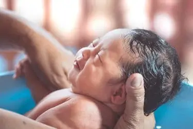 baby girl takes a bath in bathtub & Mom is cleaning her body with tenderness