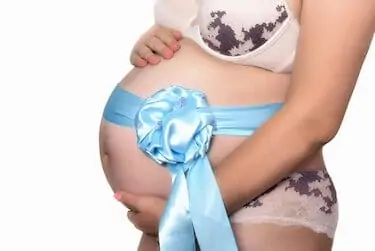 A woman happily awaits the birth of a child, bandaging her belly with a blue ribbon with a bow.