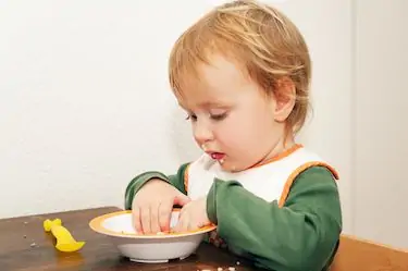 Adorable kid boy eating soup with his hands
