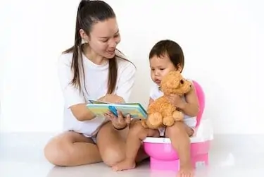 Mother teaching child to potty train while reading a book