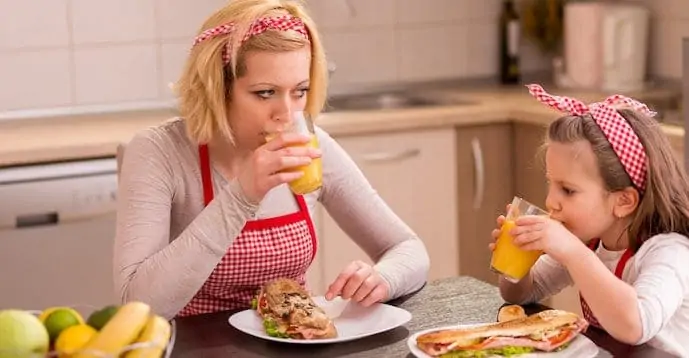 Mom and kids eating sandwiches and drinking orange juice on the table