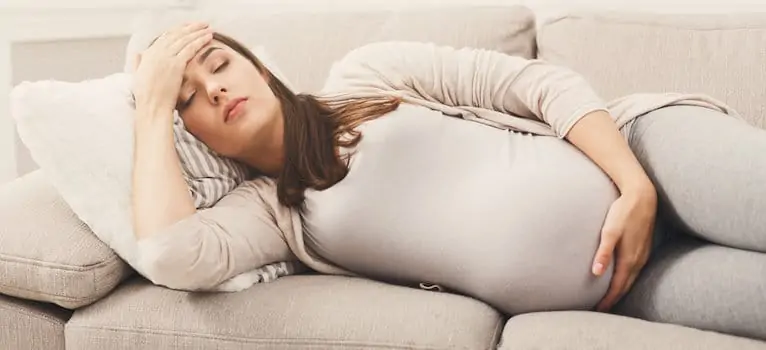 Young pregnant woman with headache lying on sofa