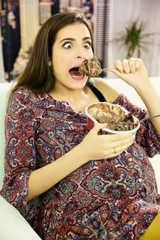 pregnant funny young woman can't resist devouring a big spoon of ice cream.