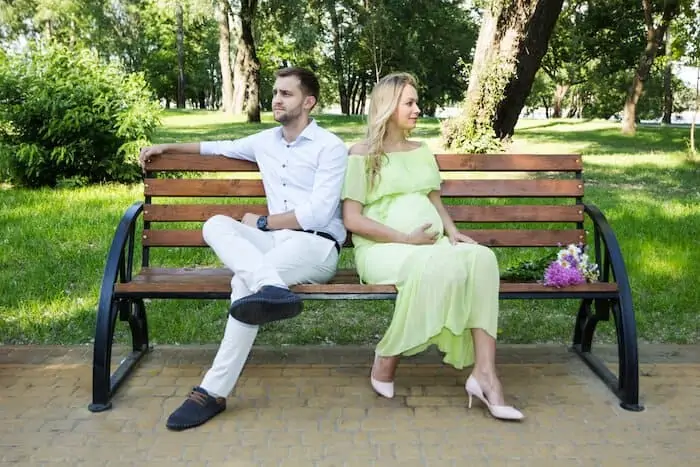 A pregnant wife and husband on a bench in the park, a quarrel.