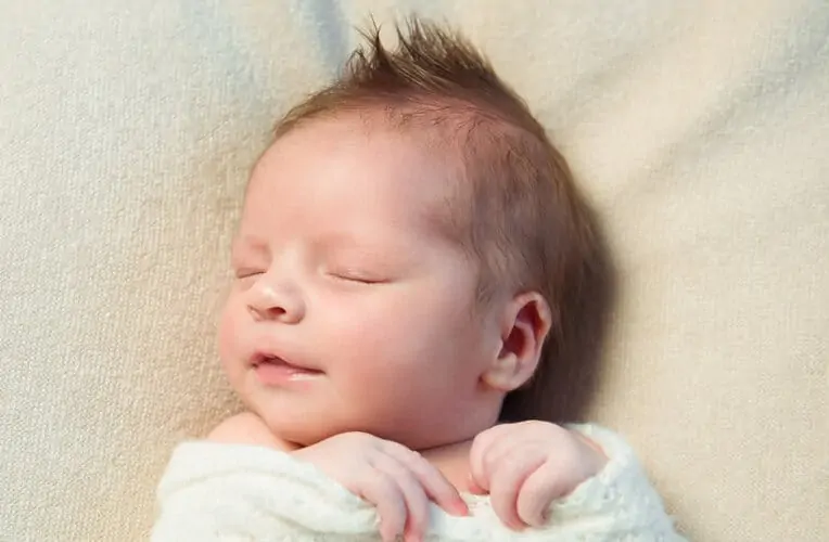 Newborn with Mohawk hair sleeping in white blanket.