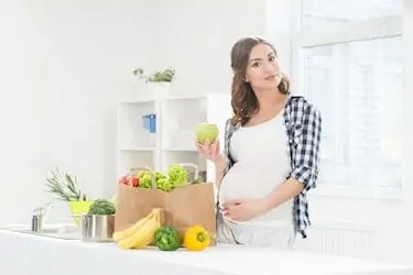 Beautiful pregnant woman in the kitchen with shopping bag and apple.