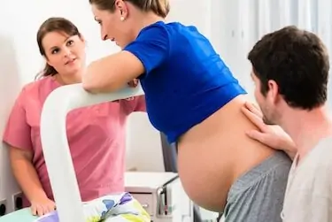 Woman laboring in delivery room with nurse and husband before birth.