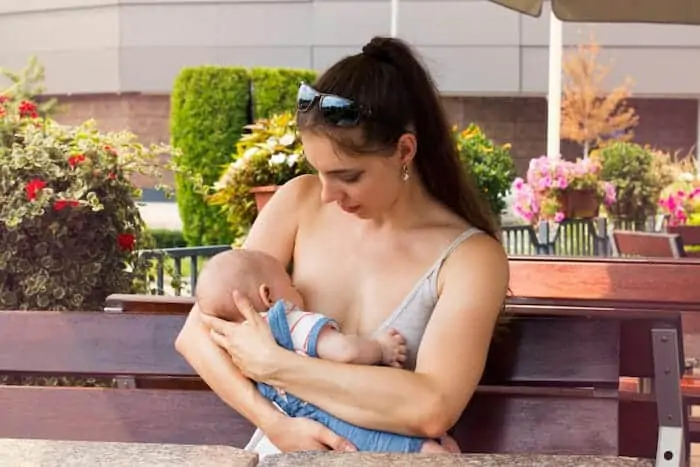 pretty mom is with newborn baby outside and breastfeeding