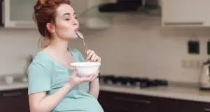 Beautiful pregnant woman eating with lust cereals on breakfast, enjoying meal.