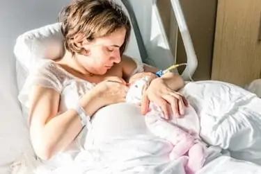 Mom breastfeeds newborn baby girl in hospital bed