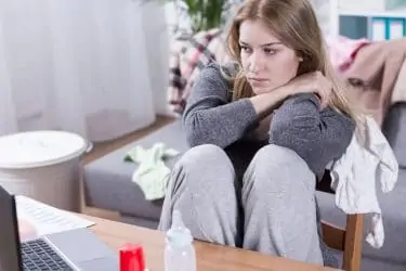 Sad and tired woman looking on laptop, sitting in messy room