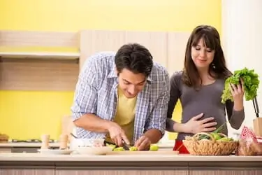 Man and pregnant woman preparing salad in kitchen