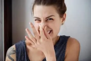 Woman pinches nose with fingers hands looks with disgust something stinks bad smell situation