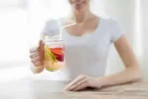 Happy woman holding glass with fruit water at home