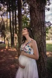 Pregnant woman stands under tree